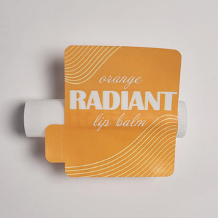 Orange lip balm container with 'Radiant' text on a light gray background