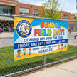 School field day banner on a chain-link fence with a school building in the background