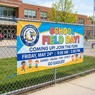 School field day banner on a chain-link fence with a school building in the background