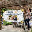 Woman hanging a 'Happy 50th Wedding Anniversary!' banner with a photo of an elderly couple outdoors.