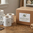 Rolls of paper and a cardboard box with 'Artisan's Nest Creations' branding on a wooden surface.
