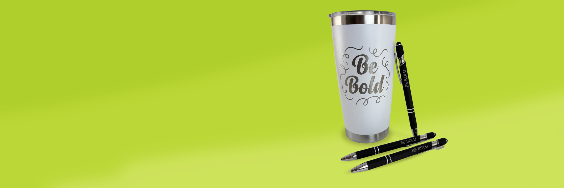 White tumbler with 'Be Bold!' text and three pens on a green background