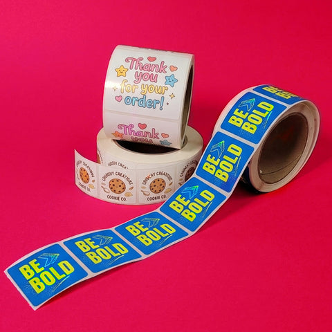 Two rolls of stickers with text and graphics on a pink background