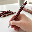Hand holding a maroon pen with silver accents, personalized with text, on a light surface.