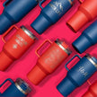 Collection of red and blue insulated drink containers on a pink background