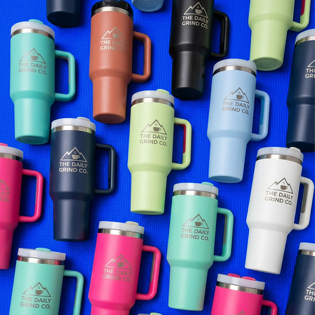 Collection of colorful insulated mugs with 'The Daily Grind Co.' logo on a blue background