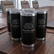 Set of black tumblers with Technovate Solutions logo on a wooden table.
